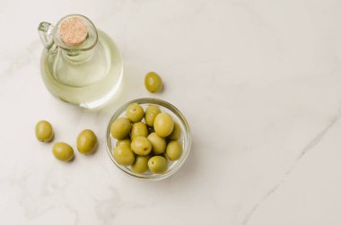 Beyaz taş masada zeytin yağı şişesi ve zeytin. Üst görünüm ve boşluk kopyala. Şişede zeytin yağı ve fiyonkta zeytin meyvesi