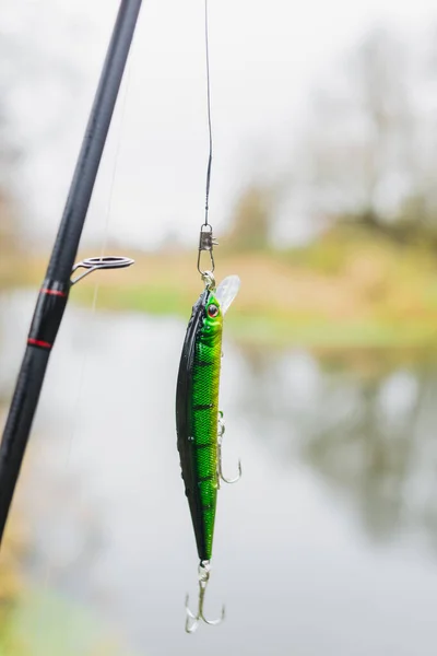 Green striped wobbler for fishing on the background of the river. Tackle for fishing. Fishing wobbler. Hobie fishing in nature