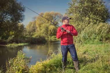 Nehir kıyısındaki adam bir döner çubuk fırlatır. Spor balıkçılığı. Güneşli bir günde balık tutmak
