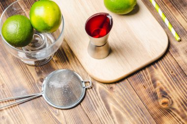 Kırmızı kokteyl yapmak için aletler. Dispanser, şişe, süzgeç ve limon. Tahta bir masanın en üst görüntüsü..