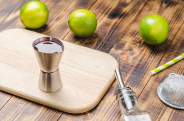 Ahşap masaya kokteyl yapmak için gerekli malzemeler. Dispanser, şişe, süzgeç ve limonlar ahşap bir masada.