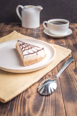 Kahveli ve kremalı tatlı. Koyu ahşap bir masada beyaz bir tabakta..