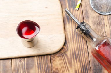 Kırmızı kokteyl yapmak için aletler. Dispanser, şişe ve elek. Tahta bir masanın en üst görüntüsü..