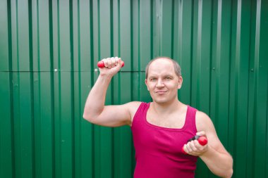 Yeşil metal arka planda dambıllarla çalışan adam..