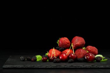 Böğürtlenler yakın plan. Stüdyoda koyu taşlı arka planda rengarenk karışımlar var.