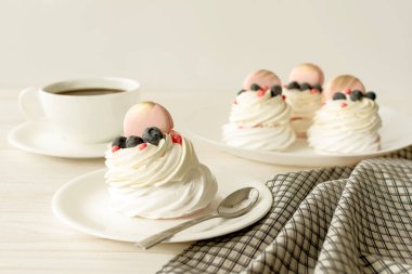 Hayat boyu Pavlova kremalı pasta, beyaz arka planda süslemeli makaron. Çay fincanları ve peçeteler ahşap masada.