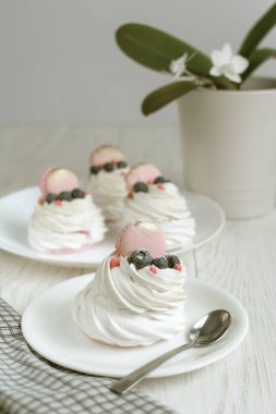 Hayat boyu Pavlova kremalı pasta, beyaz arka planda süslemeli makaron. Beyaz orkide ve tahta masanın üzerinde peçete.