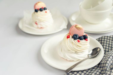 Hayat boyu Pavlova kremalı pasta, beyaz arka planda süslemeli makaron. Çay fincanları ve peçeteler ahşap masada.