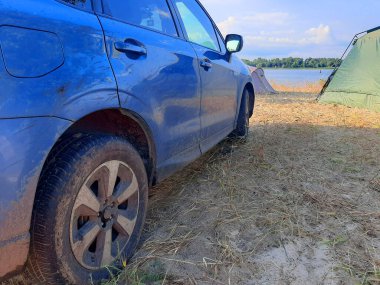 Kamp alanı yakınlarındaki nehir kıyısındaki SUV off-road araba tekerleğine bakın.