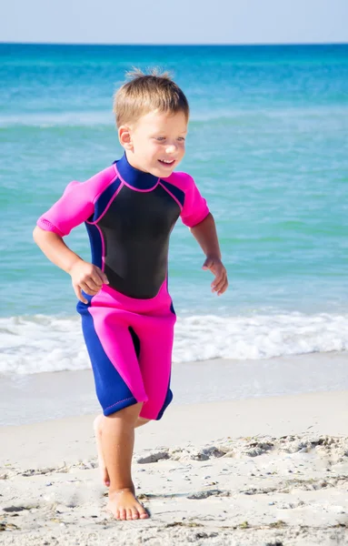 Kid i sin dykardräkt lämnar vattnet på stranden — Stockfoto