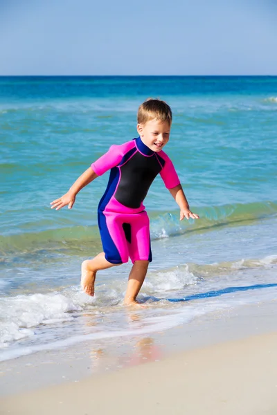 Kid i sin dykardräkt lämnar vattnet på stranden — Stockfoto