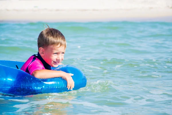 Menino feliz curtindo nadar no mar com anel de borracha — Fotografia de Stock