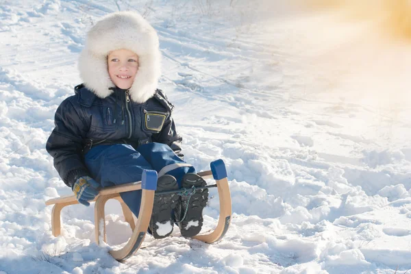 Söt ung pojke skrattar som han pulka störtlopp i snön — Stockfoto
