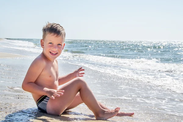 Bonito menino sentado na praia do oceano — Fotografia de Stock