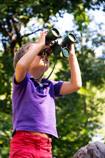 Boy looks through binoculars in forest — Stock Photo, Image