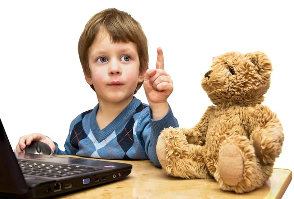 O menino ensina brinquedo urso na frente do laptop — Fotografia de Stock