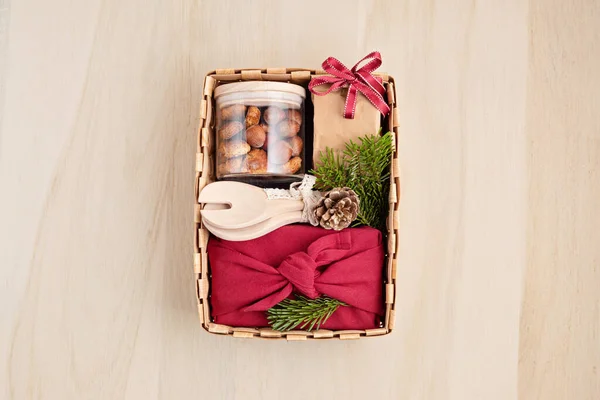 Preparing care package, seasonal gift box with kitchen utensils, furoshiki box and cookies. Personalized eco friendly basket for winter holidays. Top view, flat lay