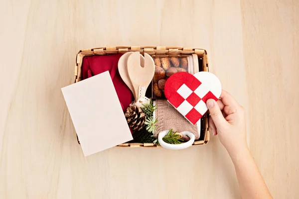 Preparing care package, sasonal gift box with kitchen utensils, furoshiki box and cookies. Personalized eco friendly basket for winter holidays, giving tuesday concept. Top view, flat lay