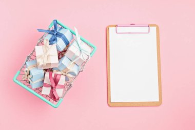 Alışveriş sepetinde Noel hediyesi kutuları ve pembe arka planda pano. Kış tatili hediye listesi maketi, fotokopi alanı olan mevsimlik alışveriş. Düz uzan, yukarıdan bak.