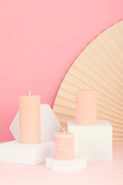 Pembe arka planda mumların ve bej yelpazenin şık sunumunun yakın çekimi. Modern minimalist doğu iç mimarisi için gül kokulu mumlar.