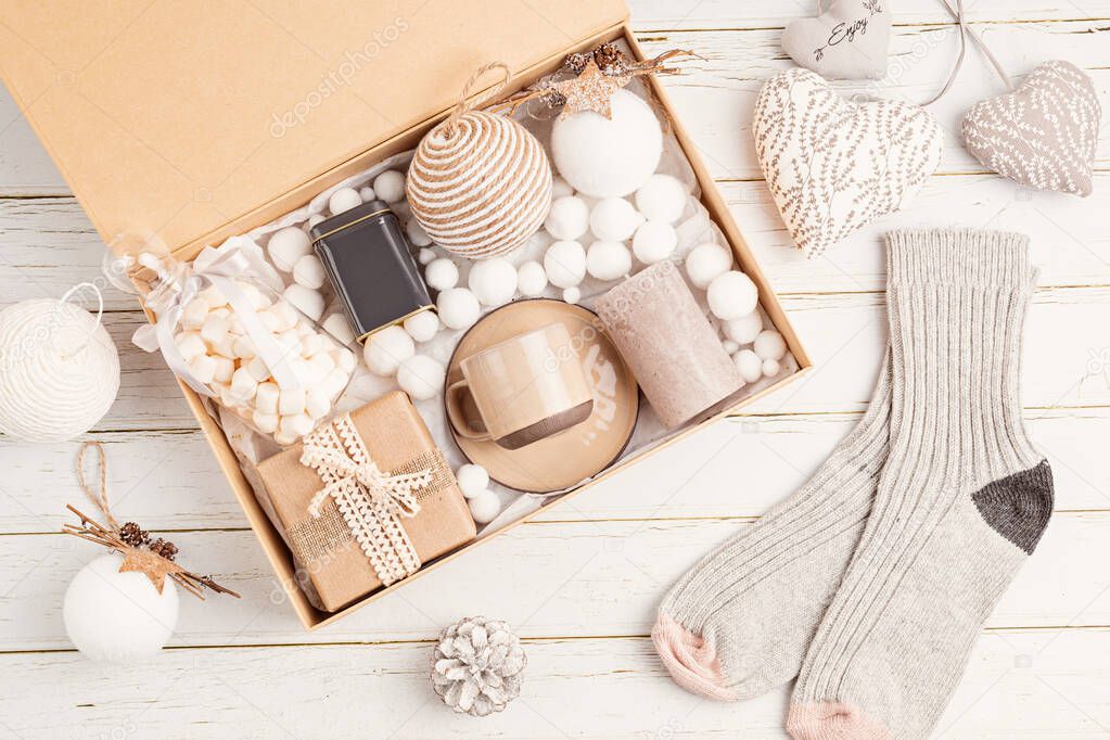 Preparing care package, seasonal gift box with tea, candle, cup and woolen socks. Personalized eco friendly basket for family and friends for christmas. Top view, flat lay