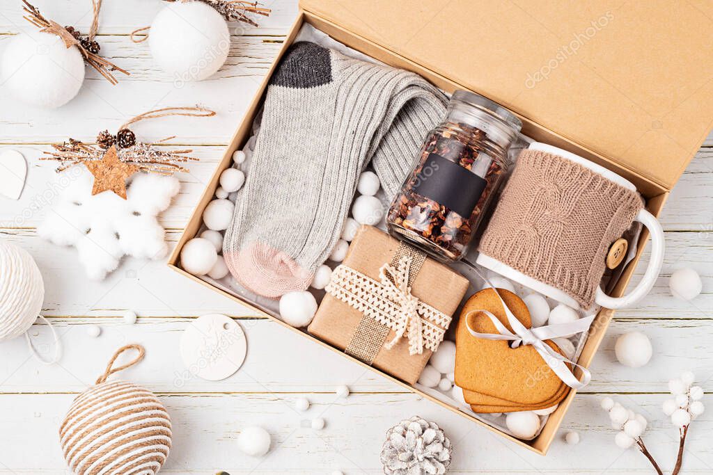 Preparing care package, seasonal gift box with tea, cookies and woolen socks. Personalized eco friendly basket for family and friends for christmas. Top view, flat lay