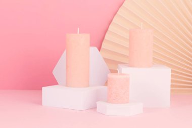 Pembe arka planda mumların ve bej yelpazenin şık sunumunun yakın çekimi. Modern minimalist doğu iç mimarisi için gül kokulu mumlar.