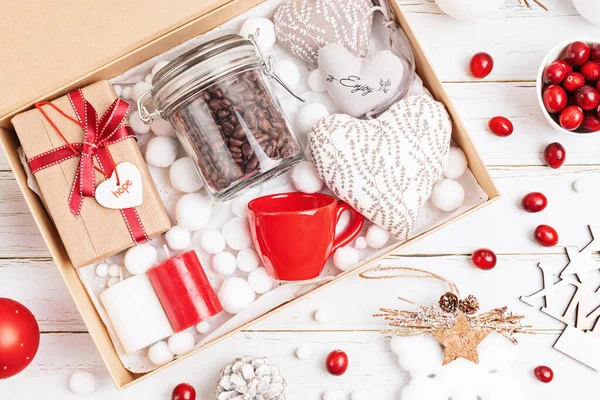 Preparing care package, seasonal gift box with coffee, candles and cup in red and white colors. Personalized eco friendly basket for family and friends for christmas. Top view, flat lay