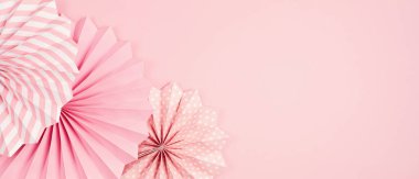 Pastel arka planda pembe kağıt çemberi hayranları olan şenlikli parti afişi. Festival, doğum günü, bebek partisi dekorasyonu. Üst görünüm