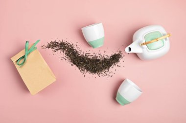 Beyaz seramik çay demliği, kuru yeşil çay yaprakları ve pembe arka planda kese kağıdı. Çevre dostu organik marka konsepti. Marka modeli. Düz yatış, üst görünüm.