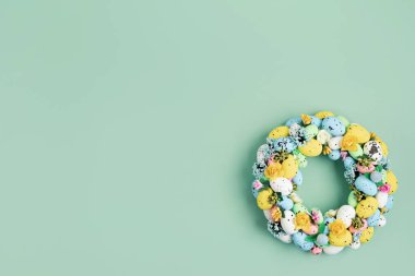 Ev yapımı iç dekorasyon çelengi ve yeşil arka planda renkli paskalya yumurtaları. Düz yatış, üst görünüm yaratıcılık zanaatı kavramı