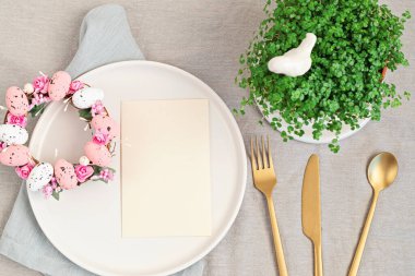Model menü ve paskalya dekorasyonuyla yatıyordu. Paskalya çelengi ve beyaz tabakta boş bir kart. Kutlama, şenlikli yemek daveti fikri