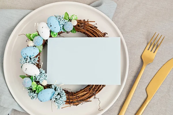 Flat lay with mockup menu and easter decoration. Easter wreath and blank card over white plate. Celebration, festive dinner invitation idea