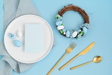 Model menü ve paskalya dekorasyonuyla yatıyordu. Paskalya çelengi ve beyaz tabakta boş bir kart. Kutlama, şenlikli yemek daveti fikri