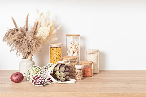 Assortment of grains, cereals and pasta in glass jars and vegetables on wooden table — Stock Photo, Image