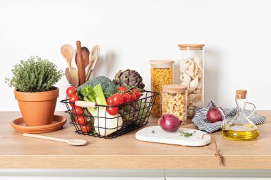 Cam kavanozlarda makarna, zeytinyağı, sebze ve mutfak aletleri ahşap masada.