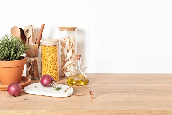 Assortment of pasta in glass jars, olive oil, vegetables and kitchen utensils on wooden table — Stock Photo, Image