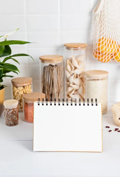 Cuaderno en blanco y surtido de granos, cereales y pasta en frascos de vidrio y utensilios de cocina — Foto de Stock