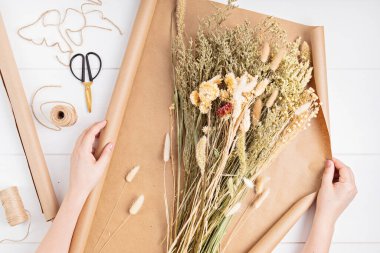 Kuru çiçek ve bitkilerden oluşan bir buket besteleyen çiçekçi.