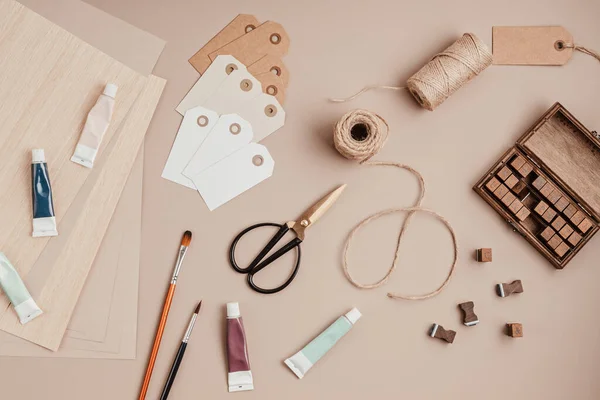 Stamp alphabet, paint, brushes, scissors and gift tags over beige background — Stock Photo, Image