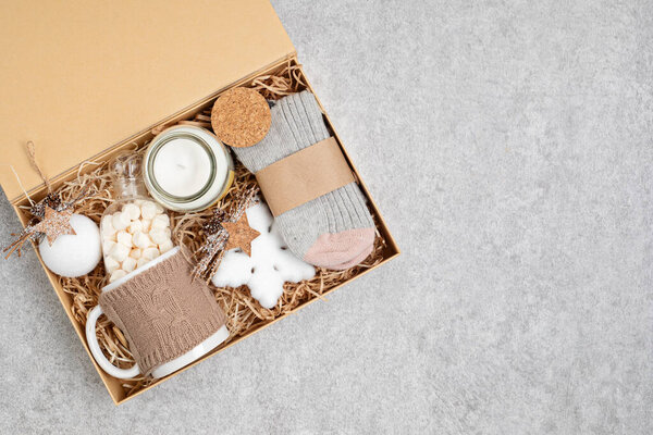 Preparing care package, seasonal gift box with mug, candle, woolen socks and christmas ornament