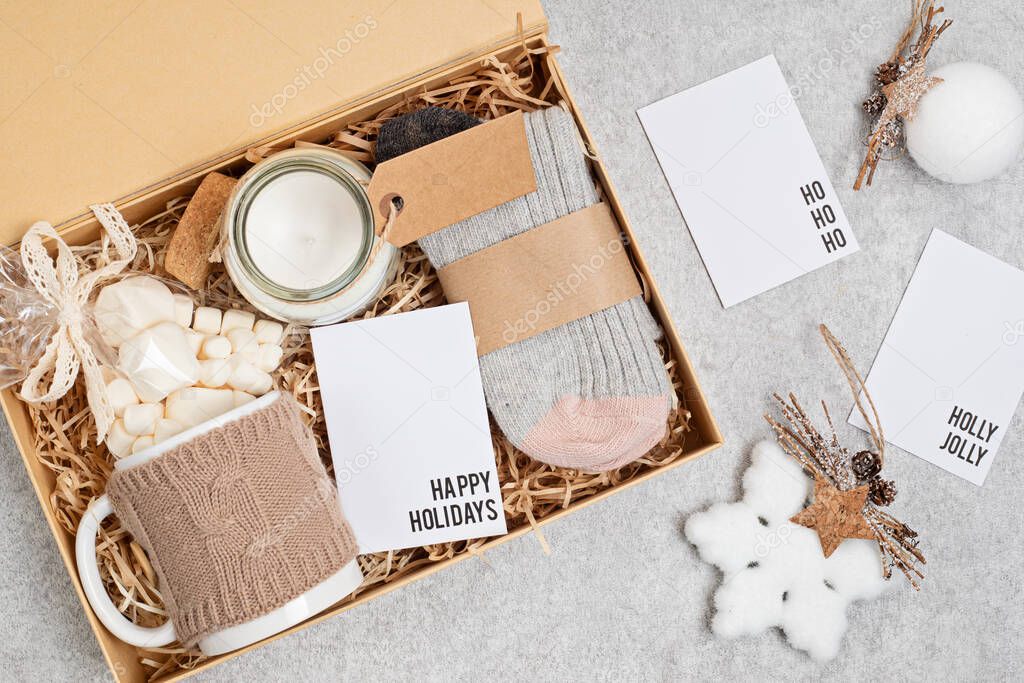 Preparing care package, seasonal gift box with mug, candle, woolen socks and christmas ornament