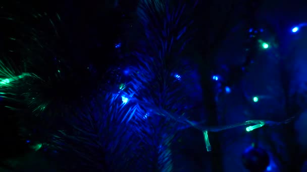 In der Nähe leuchtet ein Weihnachtsbaum, der nachts glitzert. Neujahrstanne mit Dekoration und blauer und roter Beleuchtung. — Stockvideo