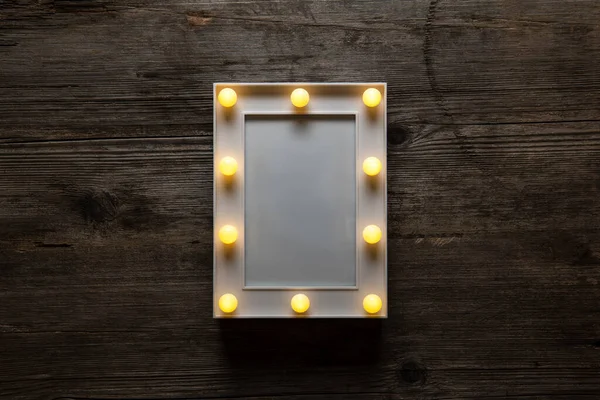 Glowing white frame with light bulbs on a vintage wooden background. Blank for postrer or postcards.