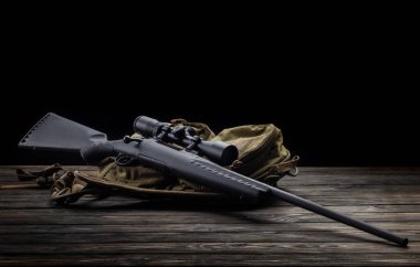 Karanlık bir arka planda teleskopik görüşlü modern sürgülü tüfek. Keskin nişancı silahı ahşap bir masada..