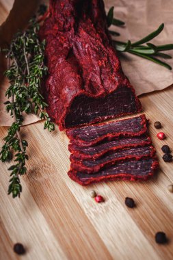 Dilimlenmiş basturma 'nın yakın çekimi. Dilimlenmiş baharatlı kurutulmuş et. Tahtada kurutulmuş at eti, biberiye ve sazan otlarıyla birlikte..