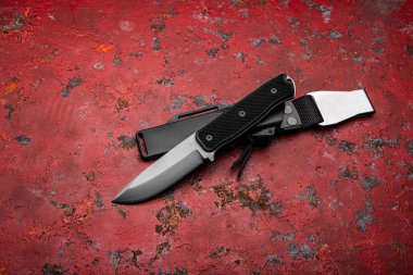 Kauçuk saplı modern bir avcı bıçağı ve kırmızı arka planda plastik bir kılıf. Nefsi müdafaa ve hayatta kalmak için silahları hazırlayın..