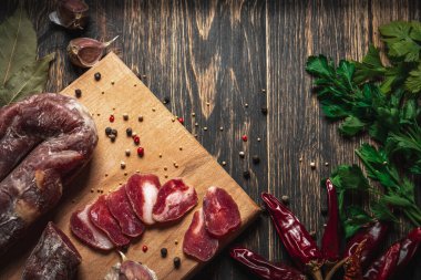 Dilimlenmiş et. Tahtada dilimlenmiş sosis çubuğu. Sarımsaklı kırmızı biber ve yeşil maydanoz..