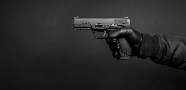 A man\'s hand in a black leather glove holds a pistol. Weapon in the hand of a man on a dark background. Weapon threat.