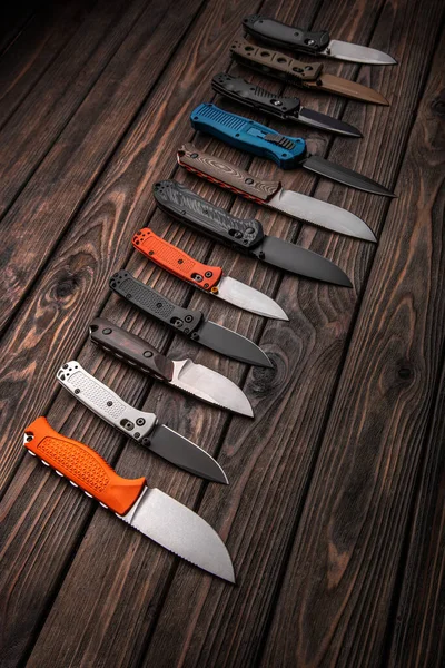 Folding knives and knives lie in a row on a brown wooden background. Various knives for hunting, sports and recreation on a wooden background.